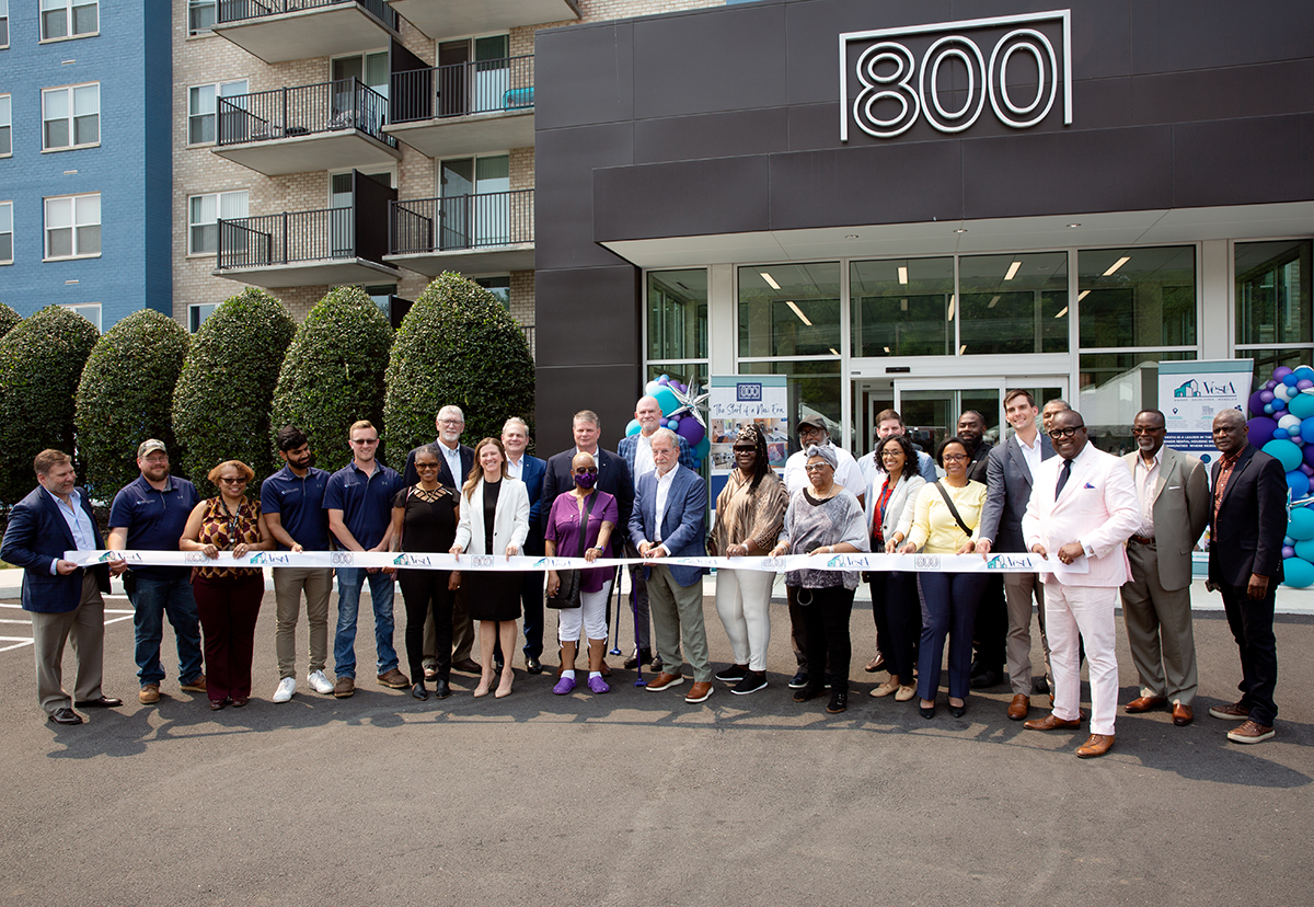 A group of Vesta employees and community leaders stand in front of the entrance to 800 Southern Avenue waiting to cut the ribbon for the reopening.
